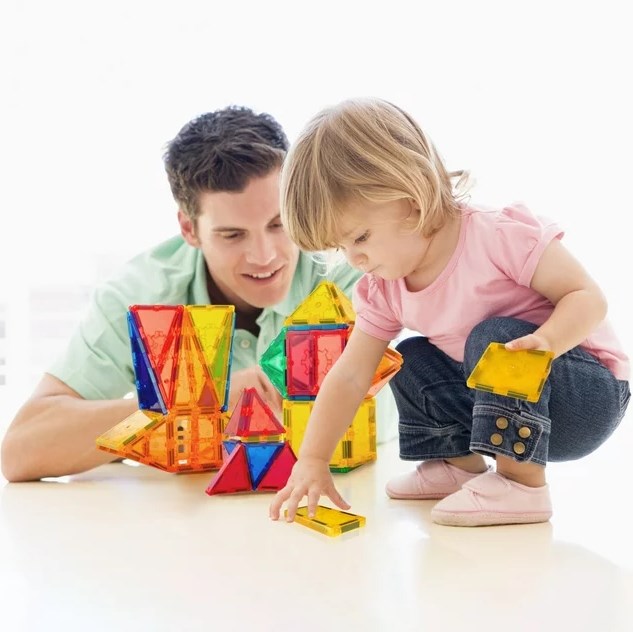 A man and a child playing with a set of magnetic blocks.