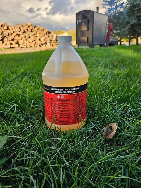 A gallon of liquid in the grass next to a pile of wood.
