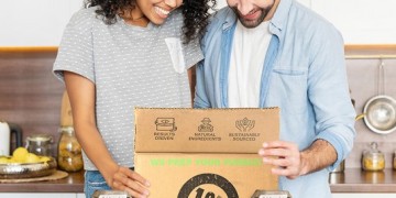 A man and woman standing in front of a box of food.