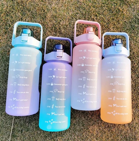 Four large water bottles with hourly drinking markers on grass.