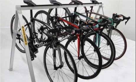 Four bicycles parked horizontally on a metal rack, featuring road bikes with slender tires and drop handlebars.