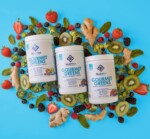 Three containers labeled "Gourmet Greens" from Nuethix are surrounded by an assortment of fruits, vegetables, and ginger on a blue background.